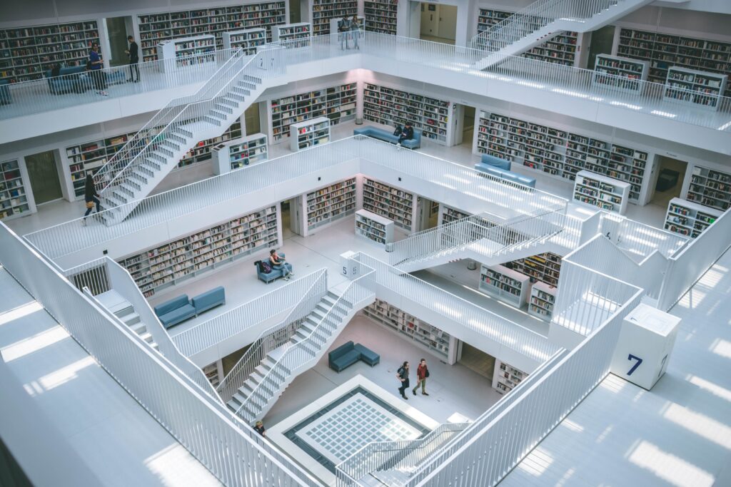 A wide open stairwell in white with many different levels. The walls are lined with book cases, and some additional lower stand-alone book cases are placed along the walk ways. There are comfy benches. People walk, or sit and browse the books. This looks like a very inviting, quiet space.